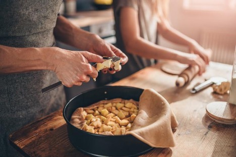 Two people preparing the ingredients for an apple pie.