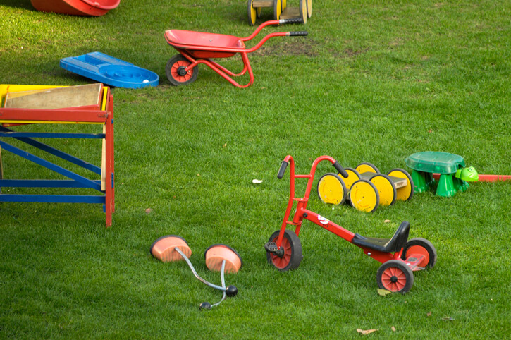 A tricycle, child’s wheelbarrow, and other toys cluttering a backyard. 